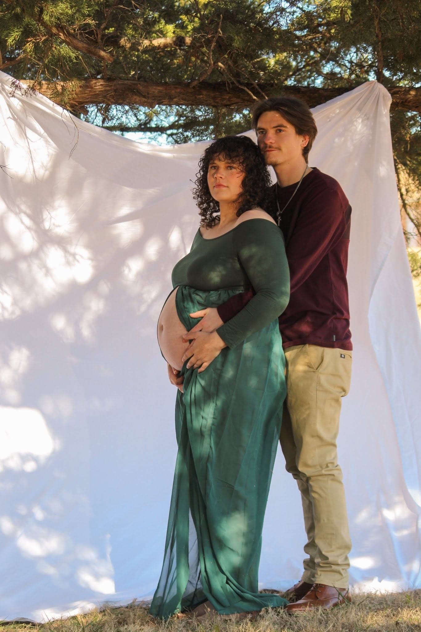 Expecting couple in front of a white sheet backdrop under the trees